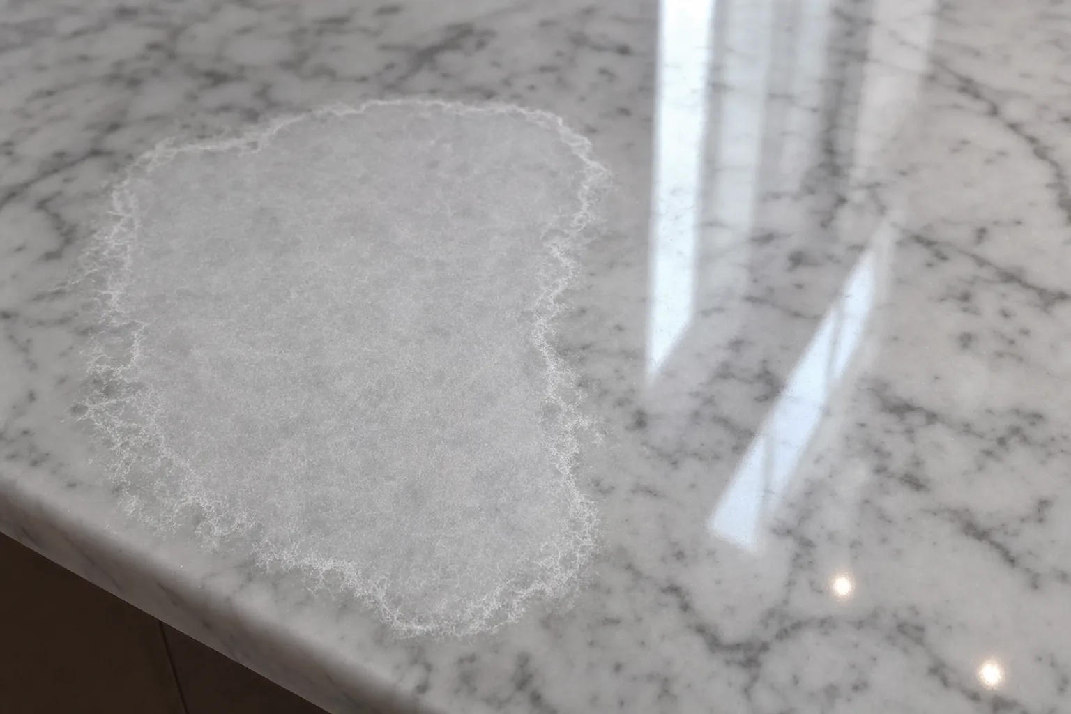 Close-up of marble countertop showing etching damage from acidic liquid creating a dull spot on the polished surface