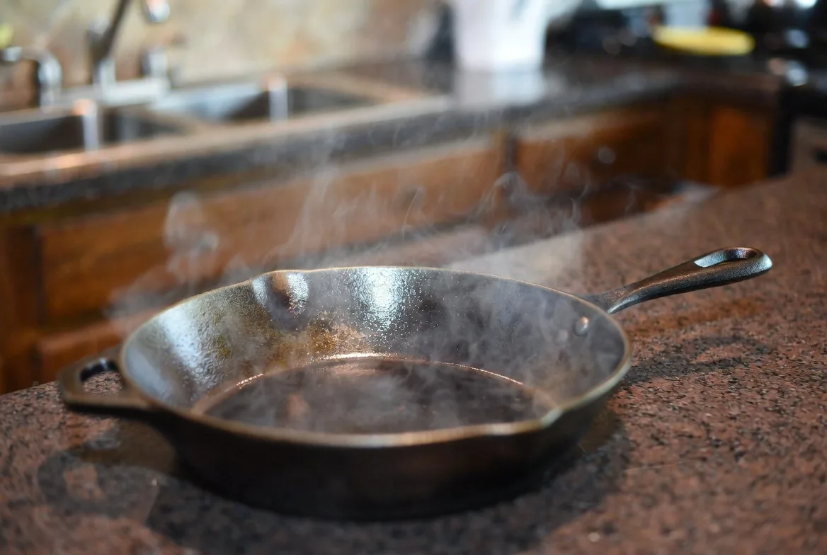 A steaming cast iron skillet resting directly on a granite countertop, demonstrating granite’s heat resistance